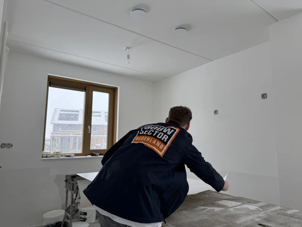 Behanger van Bouwsector Nederland legt een baan vlies op de plaktafel bij het raam