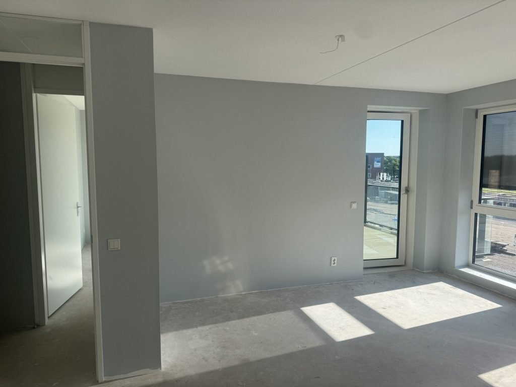 Nieuwbouwappartement met egaal gesausde lichtgrijze wanden en een betonvloer