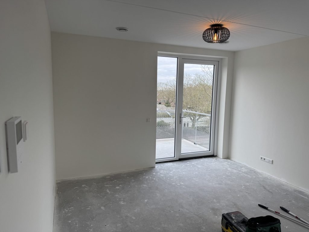 Lichte kamer met strakke wanden en openslaande deuren naar het balkon, net na het afwerken