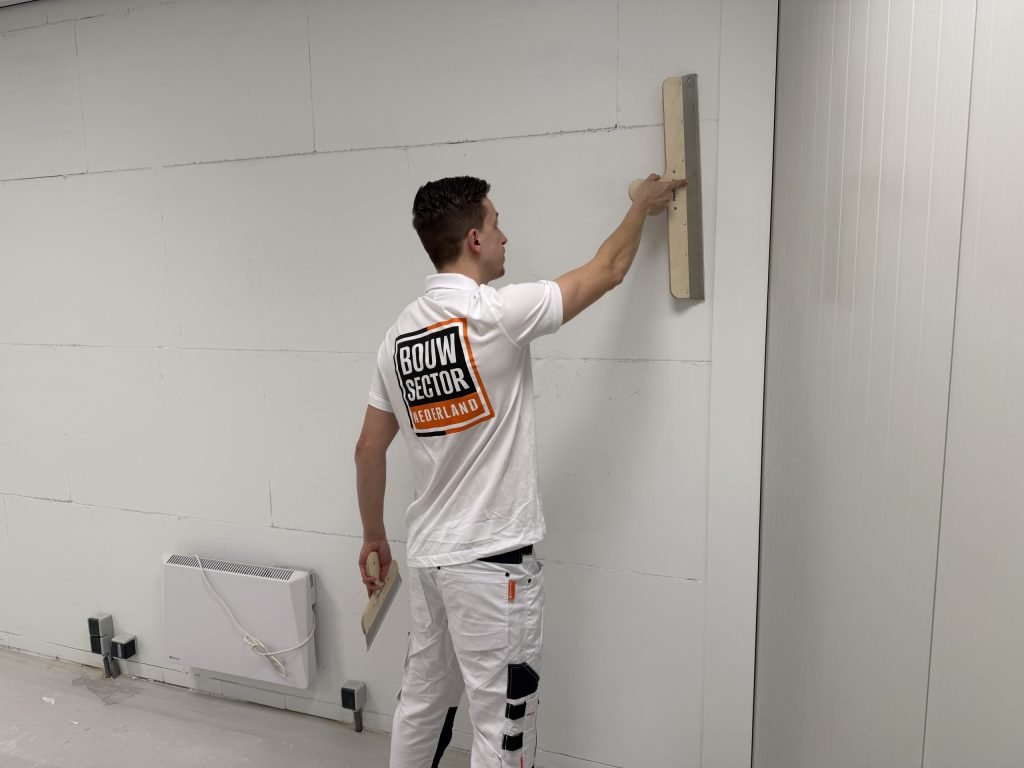 Stukadoor van Bouwsector Nederland zet een gipsplaatwand vlak met een brede spaan