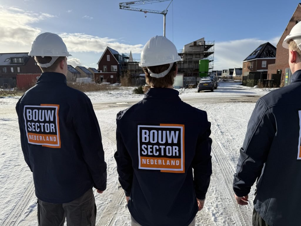 Drie vakmensen van Bouwsector Nederland met witte helm op een besneeuwde nieuwbouwplaats